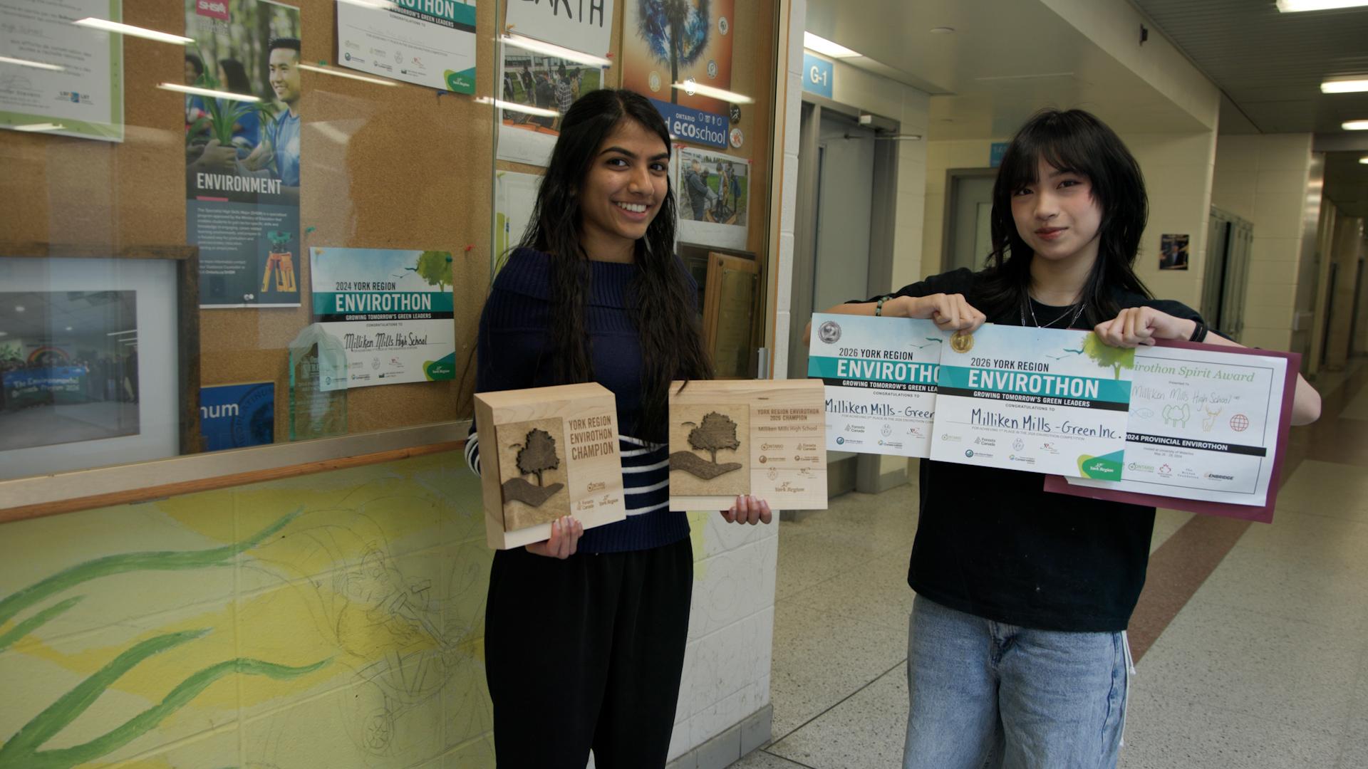 Two students stand in front of school display case holding certificates